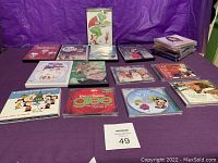 Entire lot arranged on purple fabric backdrop. Visible are several DVDs standing and laying flat with multiple CDs stacked and arranged around them.