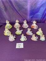 Lot of 12 vintage Josef Originals Birthday Angel figurines arranged in rows, showing a range of colors in their dresses and gold accents on wings and details.