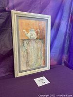 Full view of the framed watercolor painting showing the teapot on a multicolored table with warm background.