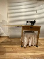 Full side view of vintage Singer Model 15-91 sewing machine on extended wood cabinet with matching stool under table