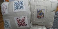 Image of two cross-stitched cushions showing detailed embroidery patterns and fabric texture.