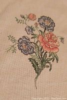 Photo shows a floral bouquet cross-stitch on cream Aida fabric with detailed stitching in blues, yellow, pinks, and greens.