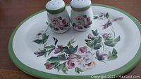 Oval floral platter with green border and raised edge, and the pair of matching salt and pepper shakers with floral rose design on a flat surface.