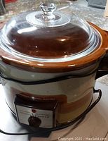 Close-up photo of General Electric crock pot showing the glass lid with knob and brown/beige exterior.