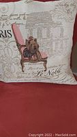 Full view of one tapestry cushion on red upholstery showing dog on pink chair design and script text.