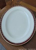 Oval vintage serving platter with maroon and gold decorative border on cream base, placed on wooden surface.