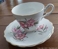 Cup and saucer set showing pink floral pattern and gold edged rims with uniquely shaped handle.
