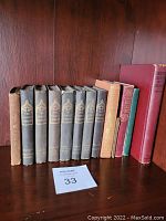 Eight volumes of The Family Library antique book series with black cloth bindings and gold embossed text, plus four additional vintage books in various colors and conditions on a wooden shelf.