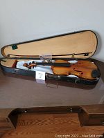 Full view of the antique violin and bow inside the wooden case, showing the fitted interior and spare parts bag.