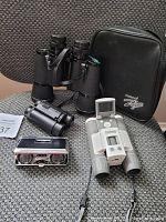 Multiple types of binoculars along with a carrying case on a patterned fabric surface.