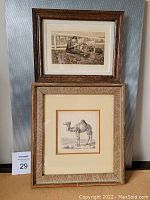 Two framed prints stacked vertically: top vintage print of two seated figures by the water, bottom print of a camel signed by L.E. Grimm in wooden frames.