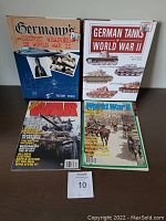Four WWII military focused items including two hardcover books about German weaponry and tanks, and two WWII magazines placed flat on a surface.
