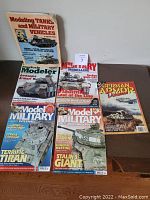 Photo showing six military modeling magazines arranged on a table with visible covers, including 'Modeling Tanks and Military Vehicles' which is the larger book standing up and several magazines laid flat.