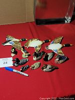Full view of all twelve miniature duck items on a red surface, showing varied styles and sizes with three larger flying ducks and nine smaller standing or resting ducks.