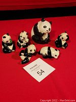 Miniature family of 6 panda ceramic figurines arranged on red background, black and white coloration, various poses including sitting, lying, holding bamboo.