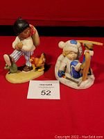 Two hand painted figurines on red background, Juan on left with chicken and cactus, Sven on right with skis