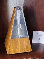 Front view of the Samick SMM 98 metronome showing wood finish and tempo scale under clear plastic.