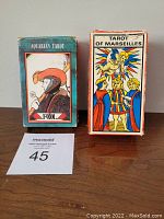Two tarot card boxes side by side: Left is 1970 Aquarian Tarot box showing artwork of 'Fool' card, right is Tarot of Marseilles box with colorful classical figure illustration, both boxes show wear with Marseilles box more damaged.