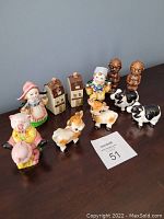 Photo of 10 ceramic hand painted salt and pepper shakers featuring animals, farmers, cottages, and tiki figures arranged on a wooden surface against a gray background.