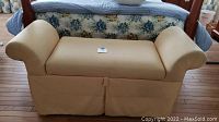 Front view of yellow padded bedroom bench with armrests and skirting to the floor.