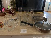 Eleven assorted beer glasses displayed including mugs and pilsner glasses with various brand logos and designs, arranged on a table surface.