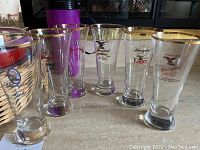 Six Yuengling beer glasses with gold rims and logo on front, arranged in a row.