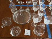 Tabletop display of various glassware items including several glasses and a glass casserole dish with lid