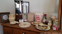 Wide view of all items including the popcorn bucket, owl vase, candles, plates, jewelry boxes, and framed wall art arranged on wood cabinet.