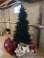 7ft artificial Christmas tree with colored lights set up in basement with assorted ornaments and tree skirts in front