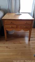 Front view of wooden end table showing drawer fronts and legs on hardwood floor.