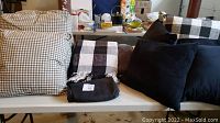 View of multiple pillows in black, white, and gray checks and solids with two blankets, one checked and one solid gray, on a table.