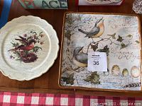 Two bird-themed serving plates, one square with birds and eggs, one round with red bird and berries, on a wooden table.
