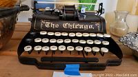 Front view of the black miniature metal typewriter with the label 'The Chicago' above the keyboard
