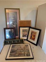 Overall collection of framed pictures, wooden shelf with pegs, mirror, and cork board arranged on and behind a table.