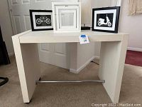 Front and angled view of a white rolling table with simple rectangular design and horizontal metal bar near the base.