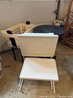 Photo of white plastic hamper with collapsible legs and two white tables in front, with round black table behind them.