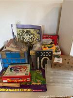 Overall view of various vintage educational games, reading materials, and art supplies organized in crates and boxes on table surface