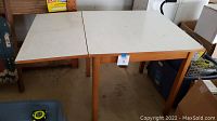 Wooden table with single drop leaf extended showing light wood legs and white surface.