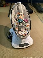 Front view of white 4moms rocker on carpet showing base, seat and power cord