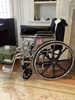 Side view of the AMG folding adult wheelchair showing padded armrests, footrests, and large rear wheels with black spokes.