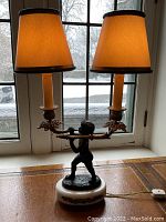 Full view of one lamp with two arms and beige fabric shade against window background
