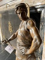 Close-up of the blacksmith’s upper torso and face showing musculature and posture