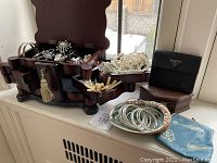 Wooden jewelry box open showing velvet compartments filled with assorted brooches, bracelets, necklaces