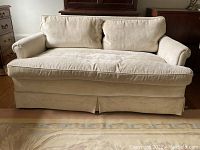 Front view of cream upholstered loveseat showing loose seat and back cushions and pleated skirt