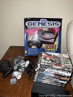 Overall lot on table: Genesis box, controllers and cables, PS2 console, PS2 game stack