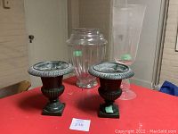 Two cast iron planters and two glass vases arranged on red tabletop