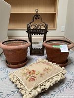 Overview of two terracotta planters, embroidered pillow, and wrought iron candle holder