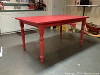 Three-quarter front view of red painted pine table in garage setting