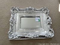 Full front view of rectangular mirror showing ornate silver-tone frame and beveled inner glass.