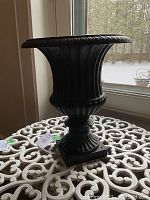 Front profile of the black cast iron urn showing overall shape and proportions on white metal table.